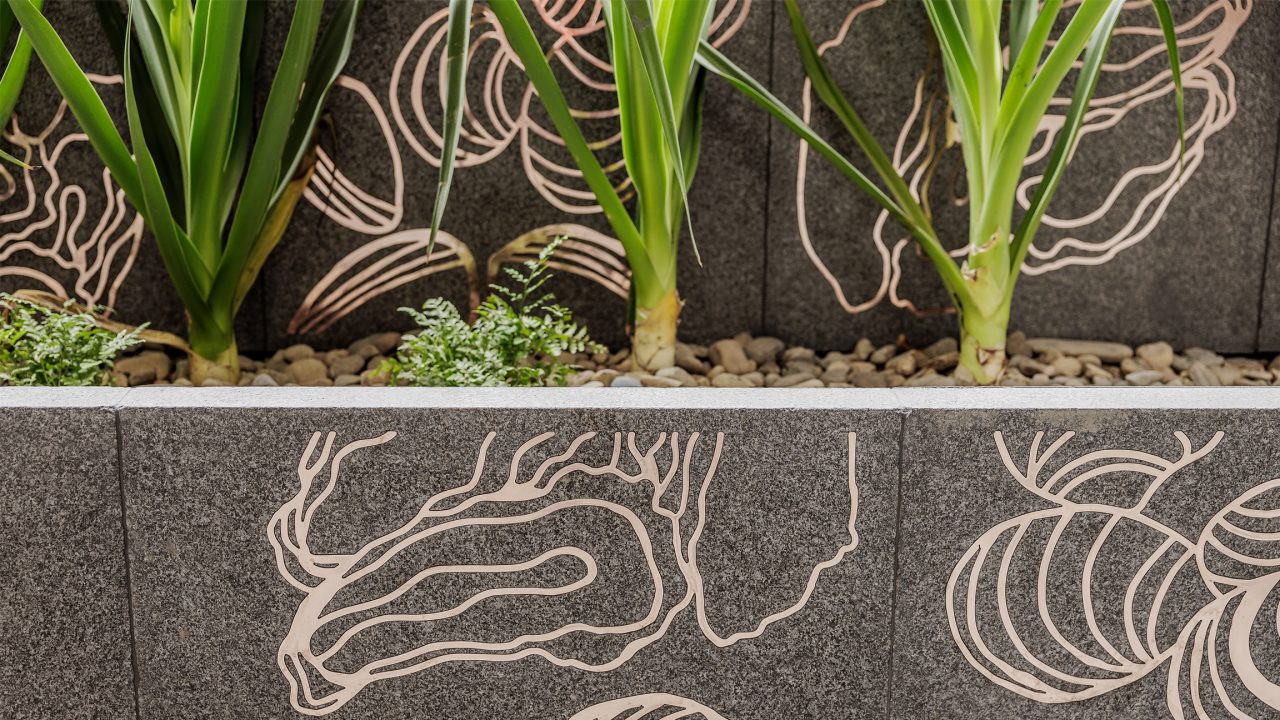 Close-up image of copper artwork inlays in stone, with native landscaping